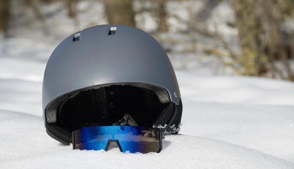 A ski helmet with goggles half-buried in snow.