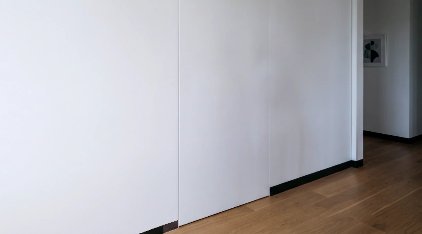 Where is the handle? A photo of a white wall with a somewhat hidden door. No way to open the door is present